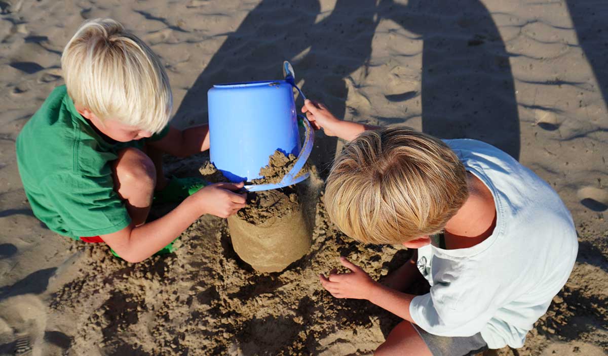 kristin holtkamp familienberatung Geschwister am strand. Kinder sind miteinander in Kontakt, bauen gemeinsam eine Sandburg.